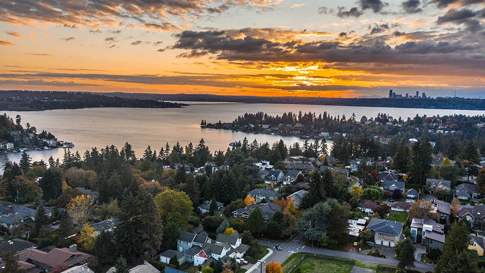 Overlooking Lake Washington and the neighborhood filled with trees. A sunset is in the background with downtown Seattle.